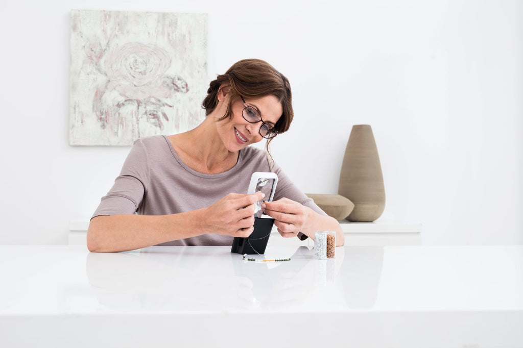 Woman using Mobilux LED with Mobase to thread a needle.